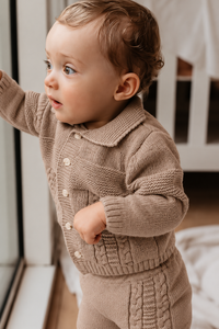 Baby in Warm Taupe gebreide babyset bij raam